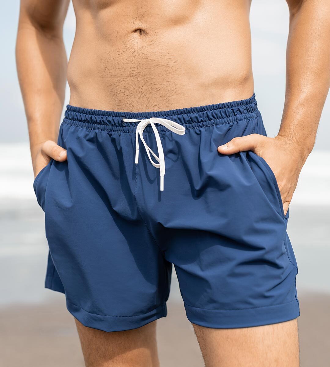 Model wearing navy men's swim shorts with a white drawstring at the beach